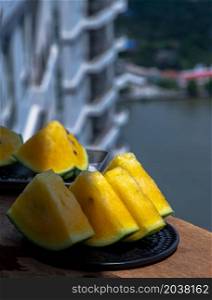 Fresh juicy yellow watermelon cut into triangles on round plate and background of buildings and city view. Tropical fruits. Select focus.