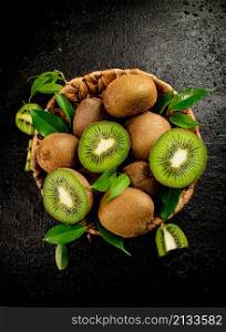 Fresh kiwi with leaves in a basket. On a black background. High quality photo. Fresh kiwi with leaves in a basket.