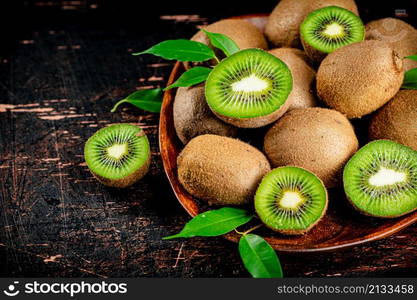 Fresh kiwi with leaves on a wooden plate. Against a dark background. High quality photo. Fresh kiwi with leaves on a wooden plate.