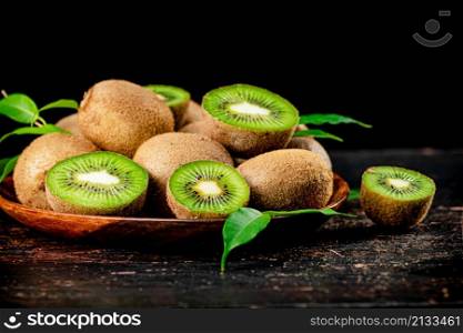 Fresh kiwi with leaves on a wooden plate. Against a dark background. High quality photo. Fresh kiwi with leaves on a wooden plate.