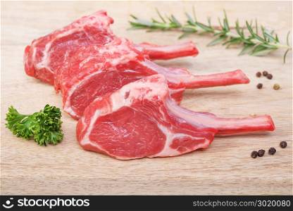 Fresh lamb cutlet with rosemary, parsley and pepper on light wooden background.
