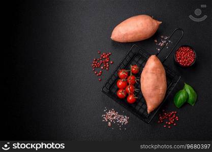 Fresh large pink sweet potato tubers with tomatoes and spices on a dark background. Cooking a healthy vegetarian meal