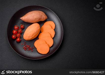 Fresh large pink sweet potato tubers with tomatoes and spices on a dark background. Cooking a healthy vegetarian meal