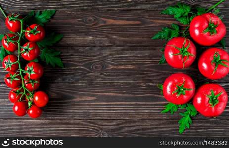Fresh large tomatoes and a branch of cherry tomatoes with leaves on a dark wooden background. Ripe tomatoes in droplets of water. Copy space for text in the center of the frame, layout