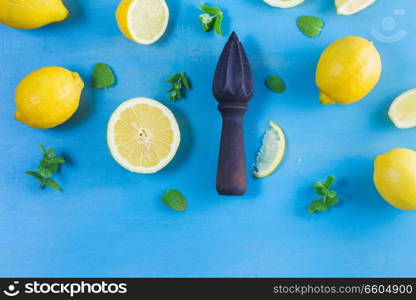 Fresh lemon citrus fruits with mint leaves and citrus reamer on blue table bakground. Fresh lemon fruits