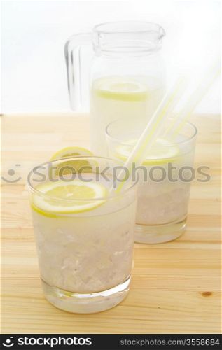 fresh lemonade drink with lemon slice closeup and pitcher carafe over pinewood table