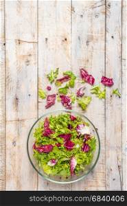 Fresh lettuce leafs mix salad in glass bowl on wooden table.