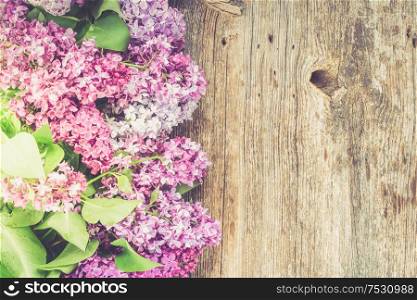 Fresh lilac flowers border over wooden background with copy space, flat lay floral composition, toned. Fresh lilac flowers