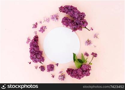 Fresh lilac flowers frame over pink background with copy space on round paper note, flat lay floral composition. Fresh lilac flowers