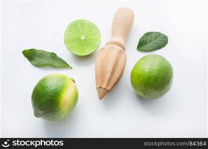 Fresh limes and wooden juicer on white background. Top view