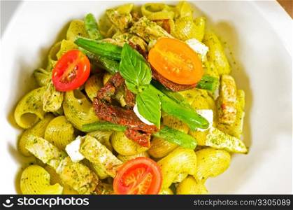 fresh lumaconi pasta and pesto sauce with vegetables and sundried tomatoes,tipycal italian food