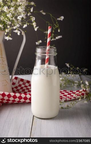 Fresh milk in glass container with red and white biodegradable stripped paper straw on wooden rustic white surface