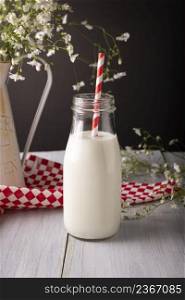 Fresh milk in glass container with red and white biodegradable stripped paper straw on wooden rustic white surface