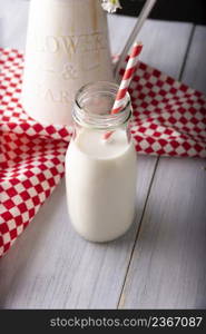 Fresh milk in little glass bottle with red and white biodegradable stripped paper straw on wooden rustic white surface