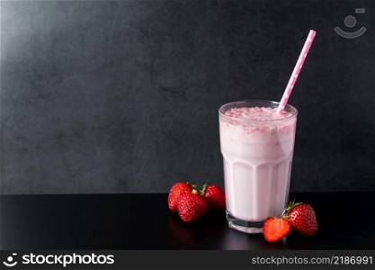 Fresh milkshake with strawberries on a black background. Summer drink with a straw in a glass. Place for text.. Fresh milkshake with strawberries on black background. Summer drink with a straw in a glass. Place for text.