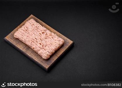 Fresh minced chicken with salt, spices and herbs on a wooden cutting board on a dark concrete background