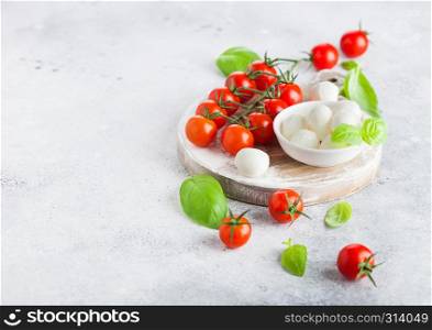 Fresh Mini Mozzarella cheese on vintage chopping board with tomatoes and basil leaf on stone kitchen background.