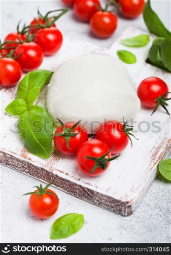 Fresh Mozzarella cheese on vintage chopping board with tomatoes and basil leaf on stone kitchen background.