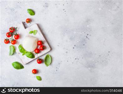 Fresh Mozzarella cheese on vintage chopping board with tomatoes and basil leaf on stone kitchen background.