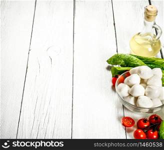 Fresh mozzarella with olive oil, tomatoes and herbs. On a white wooden background.. Fresh mozzarella with olive oil, tomatoes and herbs.