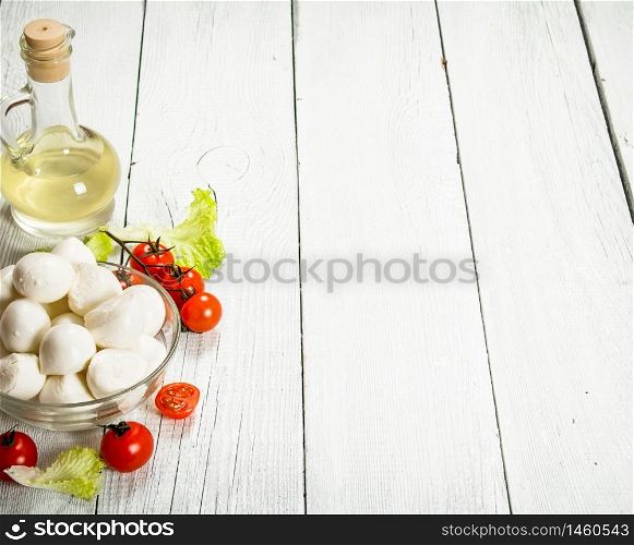 Fresh mozzarella with olive oil, tomatoes and herbs. On a white wooden background.. Fresh mozzarella with olive oil, tomatoes and herbs.