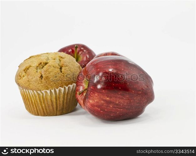 Fresh muffin is nestled among three, red apples on white background