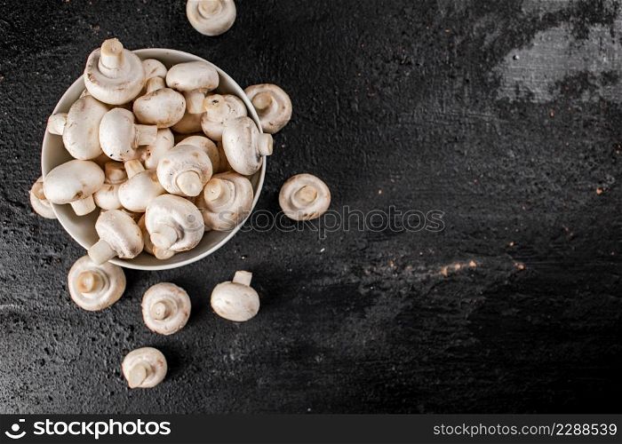 Fresh mushrooms champignons in a bowl on the table. On a black background. High quality photo. Fresh mushrooms champignons in a bowl on the table.