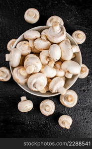 Fresh mushrooms champignons in a bowl on the table. On a black background. High quality photo. Fresh mushrooms champignons in a bowl on the table.