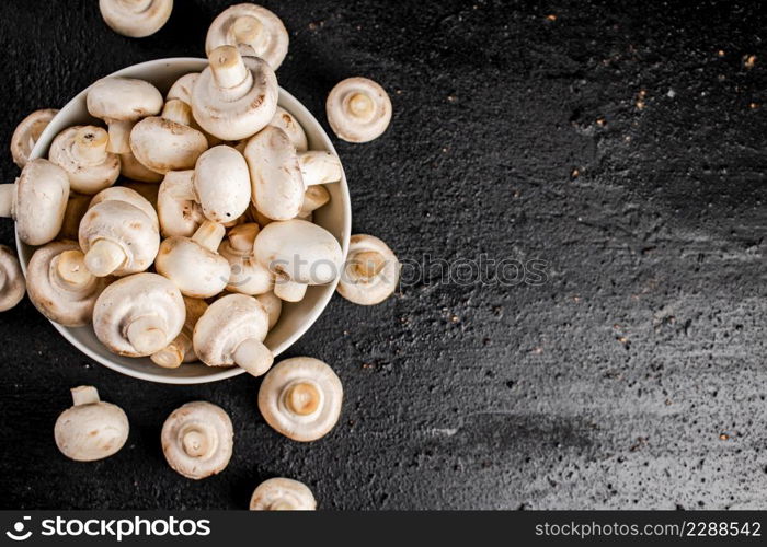 Fresh mushrooms champignons in a bowl on the table. On a black background. High quality photo. Fresh mushrooms champignons in a bowl on the table.