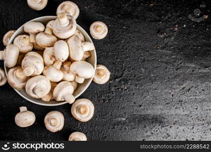 Fresh mushrooms champignons in a bowl on the table. On a black background. High quality photo. Fresh mushrooms champignons in a bowl on the table.