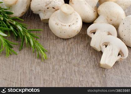 Fresh mushrooms with rosemary on a wooden background.