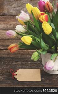 fresh muticolored tulips in white pot on wooden table with epmty tag, retro instagram toned