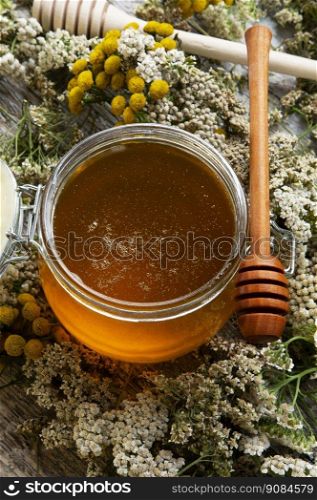 fresh natual  honey in glass jar with wooden  honey spoon around herb flowers