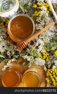 fresh natual  honey in glass jar with wooden  honey spoon around herb flowers. flat lay