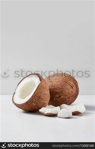 Fresh natural organic ripe whole coconut fruit with half and pieces on a light grey duotone background, copy space. Vegetarian concept.. Set from natural ripe coconut fruits with half and pieces on a grey background.