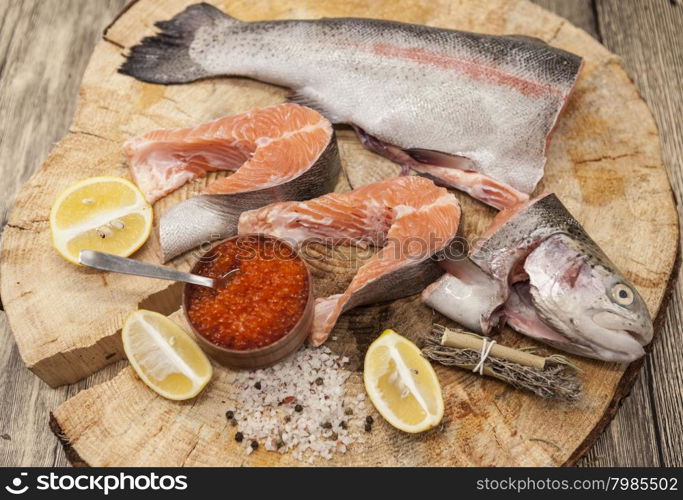 Fresh Norwegian rainbow trout with lemon red caviar, and onions on a wooden background.