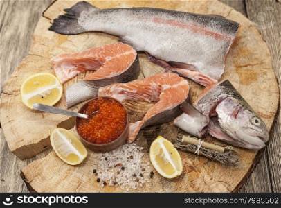 Fresh Norwegian rainbow trout with lemon red caviar, and onions on a wooden background.