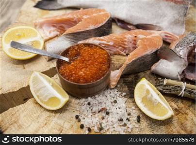 Fresh Norwegian rainbow trout with lemon red caviar, sea salt and onions on a wooden background.