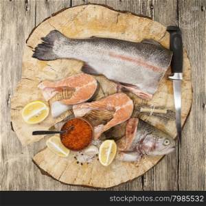 Fresh Norwegian rainbow trout with lemon red caviar, sea salt, knife and onions on a wooden background.