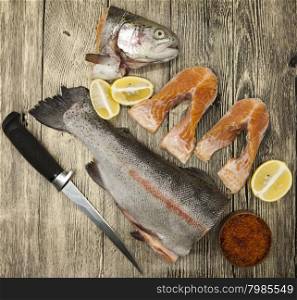 Fresh Norwegian rainbow trout with lemon red caviar, sea salt, knife and onions on a wooden background.