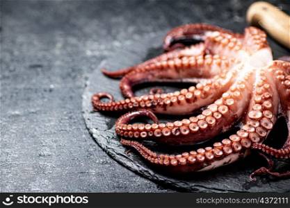 Fresh octopus on a stone board. On a black background. High quality photo. Fresh octopus on a stone board.