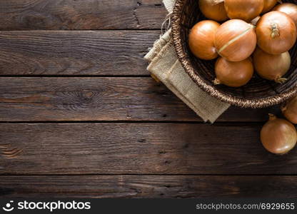 Fresh onion in basket on wooden table, top view