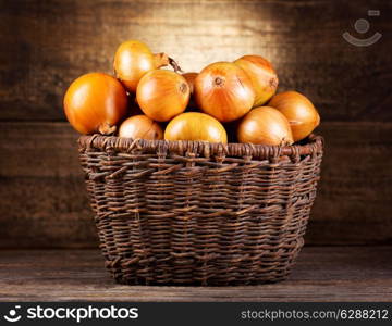 fresh onions in wicker basket on wooden background