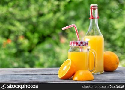 Fresh orange juice and sliced oranges on a wooden table. Natural green background. Fresh orange juice and sliced oranges on a wooden table
