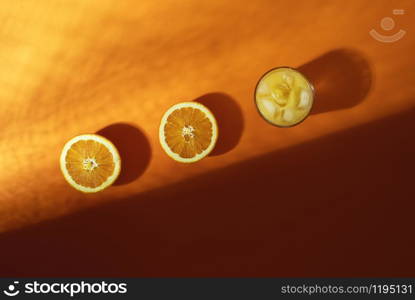 Fresh orange juice in a glass with ice cubes and orange fruit cut in halves on lush lava background, in sunlight and shadow. Cold summer drink.