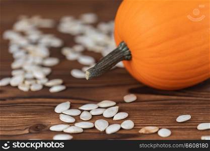Fresh orange pumpkin and pimpkin seeds close-up on wooden background. Pumpkin and seeds on wood