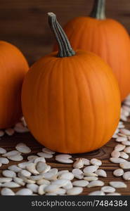 Fresh orange pumpkins and pimpkin seeds close-up on wooden background. Pumpkin seeds on wood