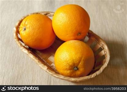 fresh oranges in the basket. three ripe oranges in the basket standing on the table