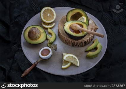 Fresh organic avocado sliced in half, Lemon sliced and Honey with Wooden stick honey dipper on Ceramic tray. Healthy food concept, Selective Focus.