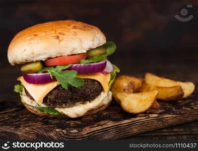 Fresh organic beef burger with cheese and sauce with vegetables and potato vedges on wooden board.